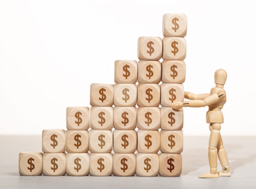 Growth, wealth or richness concept. Wooden mannequin holding a pile of wooden blocks stacked with dollar symbol