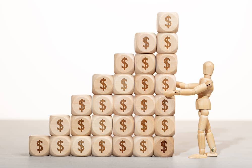 Growth, wealth or richness concept. Wooden mannequin holding a pile of wooden blocks stacked with dollar symbol