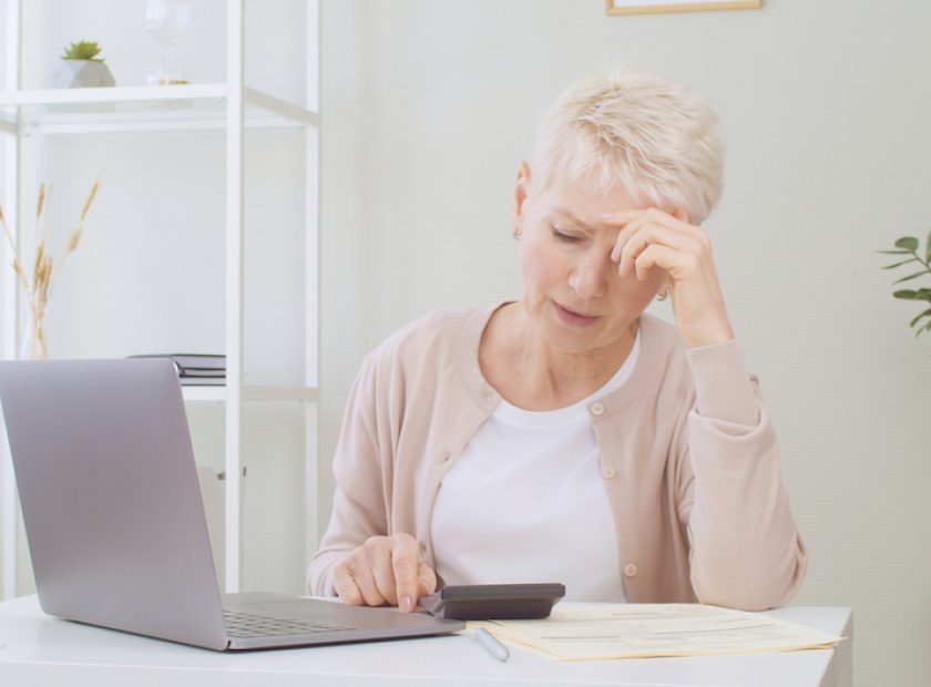 Upset senior woman sitting at table with laptop, dealing with financial stress