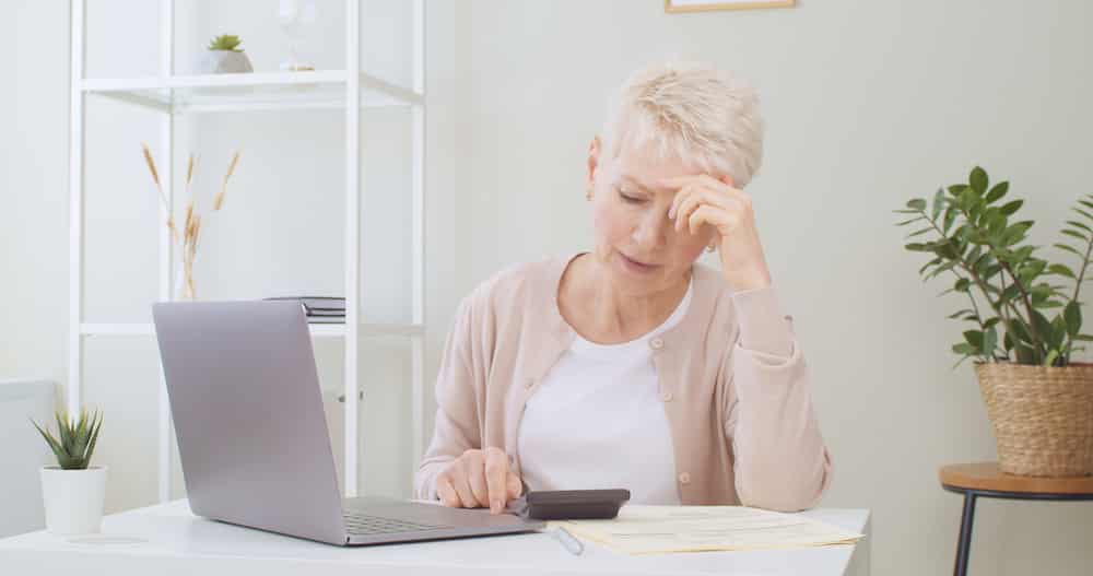 Upset senior woman sitting at table with laptop, dealing with financial stress