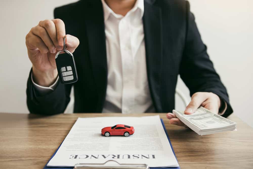 Car salespeople are holding car keys by submitting to new car buyers with car insurance concept.